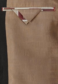 Tan fabric featuring houndstooth texture and embossed text patterns. Pocket flap with contrasting fabric edge in cream and burgundy.
