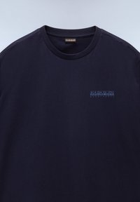 Tmavě modré bavlněné tričko s kulatým výstřihem, s malým světle modrým logem na levé straně hrudníku. Hladká textura, krátké rukávy.