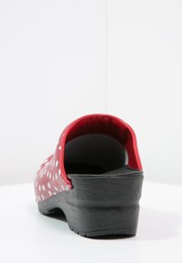 Zoccolo rosso in gomma con pois bianchi, dotato di un tallone rialzato e suola nera texturizzata. Design semplice con finitura liscia e lucida.