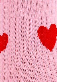 Sweter dzianinowy w kolorze różowym z czerwonymi wzorami serc. Miękka tekstura o nieco luźnym kroju, z widocznymi detalami ściągacza na całej powierzchni.