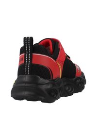 Zapato deportivo negro y rojo con parte superior de malla, suela de goma texturizada, cuello acolchado y una pestaña de tirón, con acentos amarillos.
