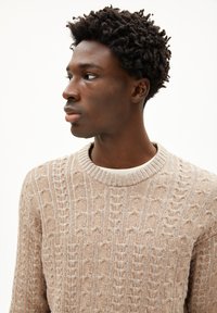 Pull en tricot beige avec un motif de cable texturé et un col rond côtelé. Tissu doux, avec de subtils accents gris clair. 