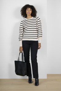Maglione a righe in crema e nero, abbinato a pantaloni neri e stivaletti. La modella tiene una borsa a tracolla nera. Tessuto strutturato, vestibilità comoda.