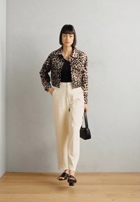 Leopardmønstret kort jakke, sort topp, beige vidbenede bukser, sort skulderveske og sorte sandaler. Glatte teksturer med distinkte mønstre.