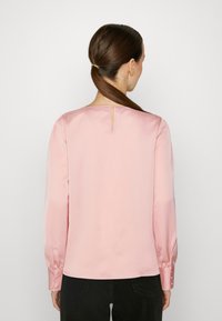 Long-sleeve blouse in soft pink satin fabric. Features a keyhole opening at the back and buttoned cuffs. Smooth, structured silhouette.