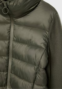 Veste matelassée vert olive avec manches tricotées, fermeture éclair devant, col montant et tirette circulaire attachée à la fermeture éclair du col.