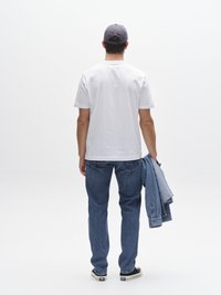 Bela majica s kratkimi rokavi, modre kavbojke iz jeansa, v roki drži svetlo modro jeans jakno in nosi siv baseball kapo, pogled od zadaj.