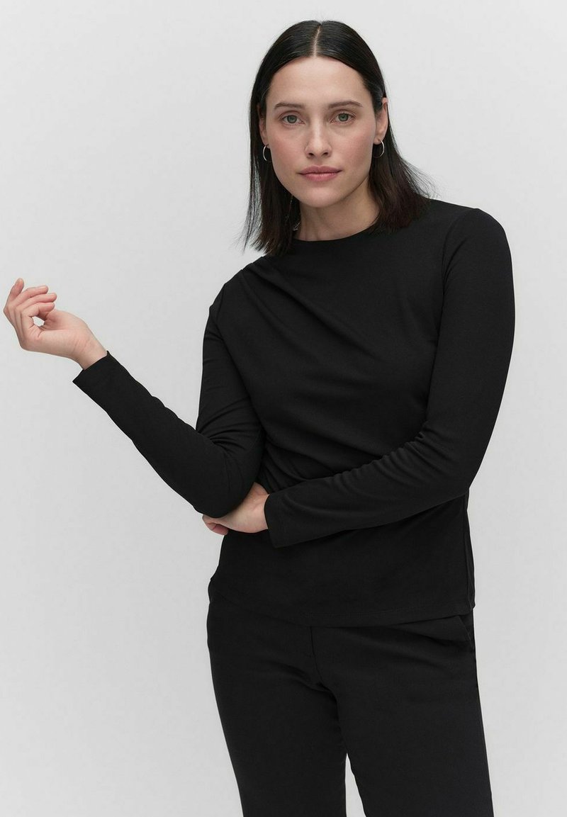 Svart långärmad topp i mjukt tyg, med hög krage och figurnära passform, tillsammans med matchande byxor. Enkelt och minimalistiskt.