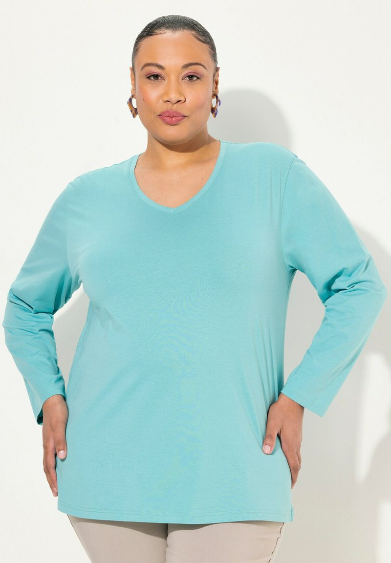 Una camicia a maniche lunghe di colore turchese con scollatura a V, realizzata in tessuto morbido, con una vestibilità rilassata e una texture liscia.