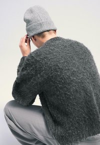 Sivý chmýričkový sveter s voľným strihom. Skombinovaný so svetlosivou rebrovanou čiapkou. Zdôrazňuje viditeľnú textúru a prírodné vlákna.