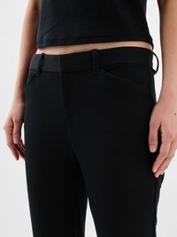 Közelkép egy személyről, aki fekete, szabott nadrágot visel övhurkokkal és egy cropped fekete toppal, kezei lazán az oldalán.