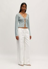 Helles blaues, geripptes Langarmshirt mit tiefem V-Ausschnitt und Knotenverschluss, kombiniert mit hochtaillierten weißen weit geschnittenen Hosen.