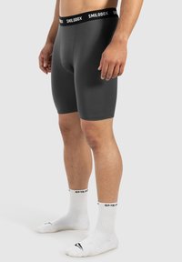 Grå atletiske boxershorts med en sort elastisk talje, der har brandet "SMILODX". Stoffet er glat og tætsiddende.