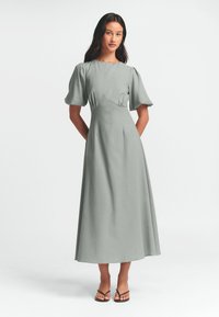 Ljusgrå, långärmad klänning med puffärmar, figurnära bodice och hel längd kjol. Slät textur, minimalistisk design.
