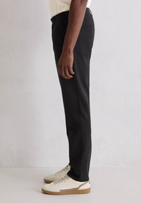 Czarne spodnie wykonane z gładkiej tkaniny o dopasowanym kroju, z klasycznym paskiem w talii i bocznymi kieszeniami, zestawione z białymi sneakersami.