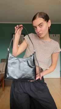 Čierna kožená crossbody taška s hladkou textúrou, zakriveným tvarom, krátkym ramenným popruhom a striebornými kovovými doplnkami. Minimalistický dizajn.