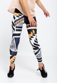 Legginsy z wysokim stanem wykonane z elastycznego materiału, z odważnymi wzorami geometrycznymi i zwierzęcymi w czarnym, pomarańczowym i białym kolorze.