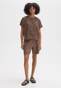 Brown striped short-sleeve shirt with a pocket, paired with light brown shorts. Worn with black sandals. Smooth fabric and relaxed fit.