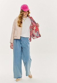 Prešívaná béžová bunda s kvetinovou podšívkou, voľné svetlomodré džíny a ružová šiltovka. Tenisky s béžovými akcentmi.