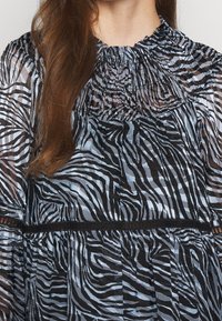 Musta ja vaaleansininen zebra-raidoitettu paita, jossa on rypytetty pääntie, teksturoitu kangas ja mustat korostukset.