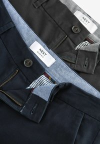 Kaks paari slim-fit pükse mustas ja tumesinisest värvist, millel on nööbid, lukud ja kontrastsed vöökummist voodrid triibuliste mustritega.