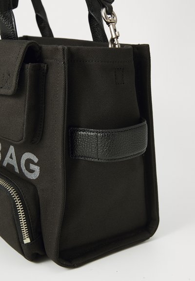 Black fabric handbag with a textured black leather accent, zippered pocket, and silver hardware. Features a sturdy handle and logo detail.