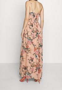 Blommig maxikjol i persikofärg med tunna axelband. Har en smockad rygg, flödande tyg och livliga blommönster i rosa och grönt.