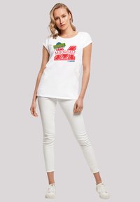 Weißes Baumwoll-T-Shirt mit rotem "MOORDALE SECONDARY" Grafik, kurze Ärmel, lockere Passform, kombiniert mit weißen Skinny-Hosen und Sneakers.