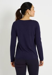 Suéter de manga larga azul marino con escote redondo y textura suave. Presenta puños y dobladillo acanalados, silueta ajustada.