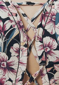 Tela de patrón floral en azul marino con flores en tonos rosa y crema; presenta un diseño de espalda cruzada con tirantes finos y bordes en un contraste negro.