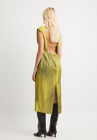 Green satin dress with a deep back cutout and side slit; features cap sleeves and a smooth texture. Paired with knee-high black boots.