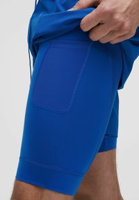 Blå sportshorts gjorda av elastisk tyg, med en sidoficka och en åtsittande design. Materialet har en slät textur.