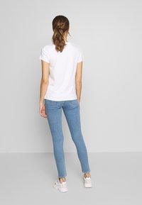 Camiseta blanca de algodón con mangas cortas, combinada con jeans ajustados de mezclilla azul claro y zapatillas blancas. Diseño simple y ajustado, sin patrones visibles.