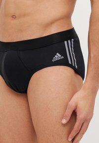 Mustat puuvillaboksereiden, joissa on joustava vyötärö, ja sivuilla on kolme harmaata raitaa sekä Adidaksen logo edessä.