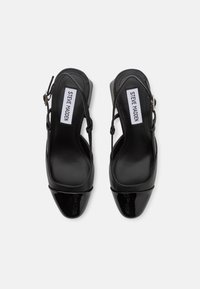 Sorte slingback hæler med en glansfull patent tåhette, glatt tekstur og en spenne-rem. Merket "Steve Madden" inni.