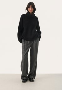 Zwarte ribgebreide coltrui met oversized mouwen, gecombineerd met grijze high-waisted, wijde broek en zwarte enkellaarsjes.