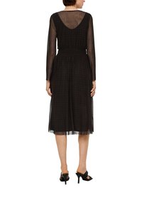 Zwarte jurk met een doorschijnende lange mouwen overlay, gerimpelde taille, middenkuit-lengte en een scoop back design. Gladde textuur met een subtiel patroon.