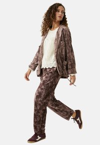 Conjunto de terciopelo en malva con un patrón texturizado; chaqueta suelta con bolsillos, combinada con pantalones estampados y zapatillas oscuras con acentos blancos.