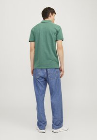 Grøn polo skjorte med en struktureret overflade, udstyret med en ribbet krave og korte ærmer, parret med løse blå denim jeans.
