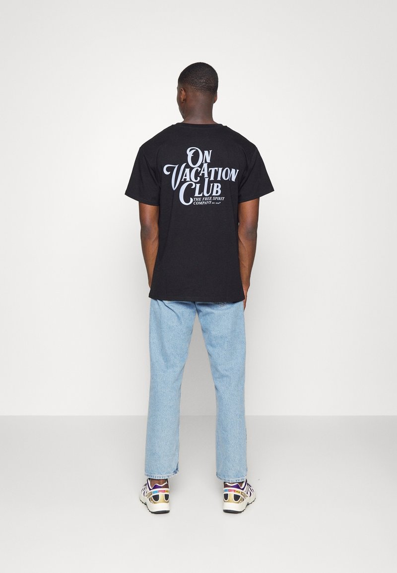 Czarna bawełniana koszulka z dużym białym napisem "ON VACATION CLUB" na plecach. W połączeniu z jasnoniebieskimi dżinsami oraz wielokolorowymi trampkami.