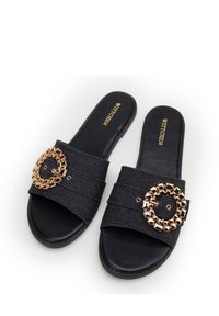 Zwarte slip-on sandalen met een textuurstof bovenkant, voorzien van een grote goudkleurige ronde versiering en een platte zool.