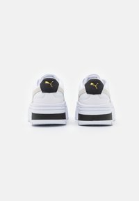 Sneaker platform bianche con accenti neri e beigi. Presentano un tallone testurizzato con un logo dorato. Suola spessa bianca con dettagli a contrasto.