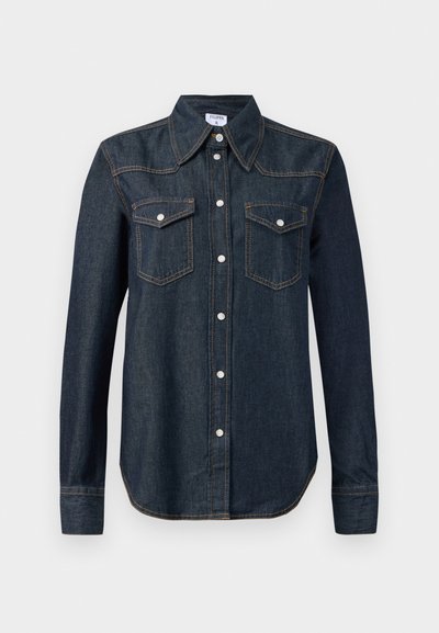 Mørkeblå denimskjorte med spiss krage, lange ermer, knappet front og to brystlommer. Har hvit søm og metallknapper.