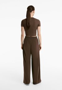 Top corto marrone con maniche corte abbinato a pantaloni palazzo a vita alta, caratterizzati da una superficie liscia e una vita elastica.