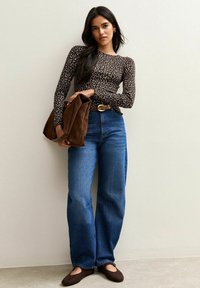 Top a maniche lunghe, aderente, con stampa leopardata, abbinato a jeans blue a vita alta e gamba larga e scarpe basse marroni, mentre tiene in mano una borsa in suede marrone.