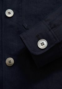 Dark navy linen shirt featuring a cuff with a silver button, four-button detailing, and a smooth texture with minimal stitching accents.