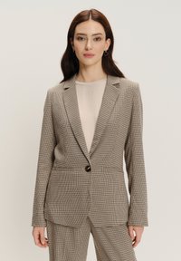 Tkaninowy blazer w beżowo-brązowe wzory w kratę, z klapami, pojedynczym zapięciem na guzik i dwiema przednimi kieszeniami.