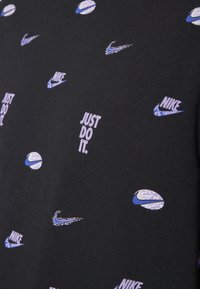 Camiseta negra de manga corta con varios logos de Nike y la frase "JUST DO IT." en blanco, con una mezcla de patrones azules y texturizados.