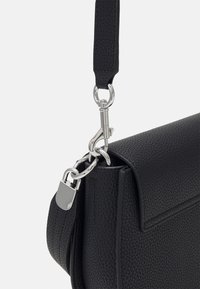 Czarna skórzana torebka o teksturowanym wykończeniu, z srebrnym zapięciem i okuciami, w strukturalnym kształcie i z odpinanym paskiem.