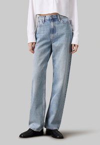 Jeans de tiro alto en denim, de pierna ancha y color azul claro, con bolsillos frontales y un ligero desgaste. Combinados con botas negras de tobillo.